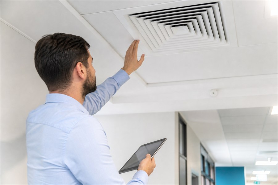 Technicien contrôlant une bouche de ventilation dans un bâtiment professionnel